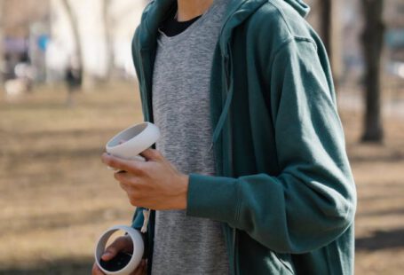 Collaborative Learning, Virtual Environment - Side view of young male in sportswear and VR headset holding controllers while standing in park in autumn