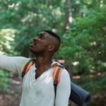 Fear, Failure - African American male with backpack standing in forest and holding mobile phone while catching GPS signal during hike