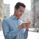 Positive Thinking, Success - Concentrated ethnic guy surfing smartphone on street