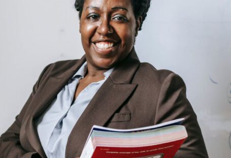 Benefits, Career Mentor - Happy black female teacher standing with workbooks near whiteboard