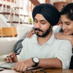 Relationships, Career Advancement - Cheerful ethnic couple using calculator while sitting at table