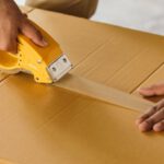 Strategies, Stand Out - Unrecognizable man sealing box with duck tape while preparing for moving out