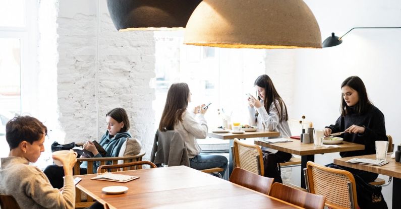 Public Speaking, Skills - Side view of group of female friends talking during lunch time and teenagers sitting at wooden table in cafe with big hanging lamps in daylight
